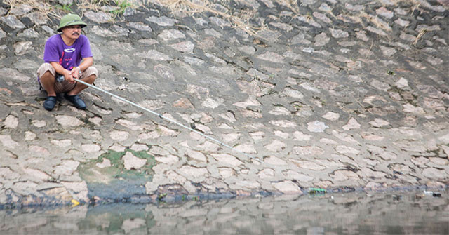 People 'leisurely' sit fishing on the banks of To Lich River